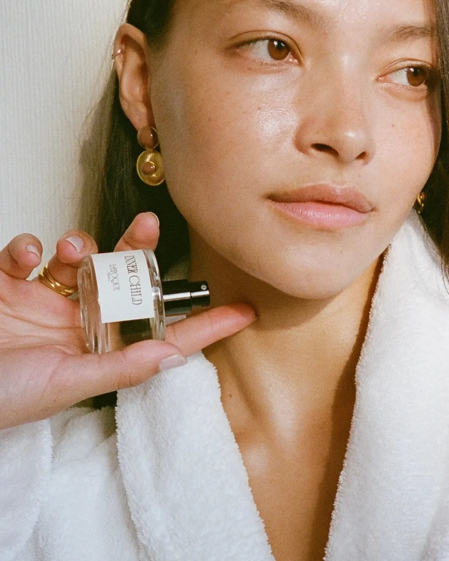 Inner Child eau de parfum 30mL by L'Epoque, held in a manicured hand against a bed of deep red roses