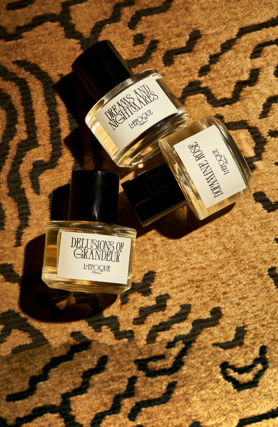 Delusions of Grandeur eau de parfum 30mL by L’Epoque, held up in a man’s hand beside a woman in a white top with red nails, cap in hand