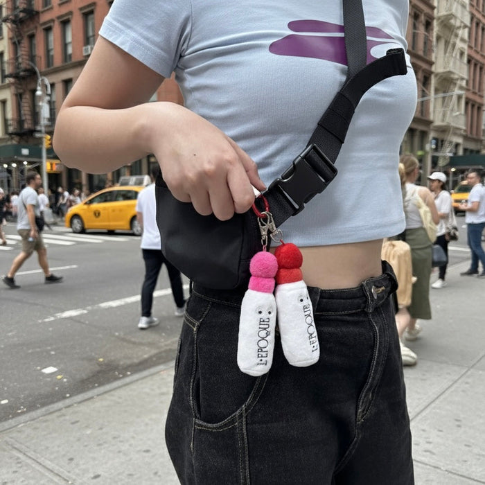 Person holding a black bag with colorful keychains on a city street.