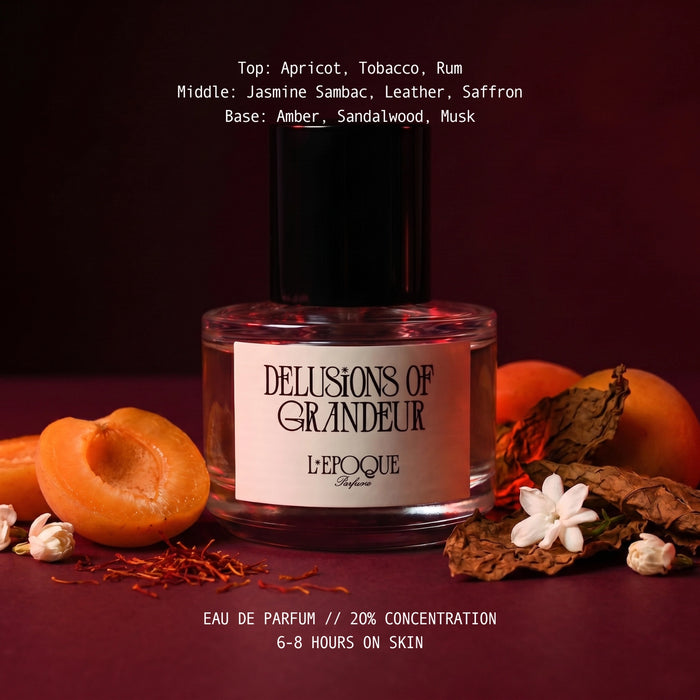 Delusions of Grandeur eau de parfum by L'Epoque surrounded by fresh apricot, saffron threads, dried tobacco leaves, and jasmine blossoms on a deep burgundy background