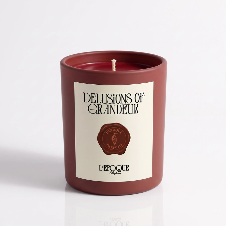 Delusions of Grandeur scented candle by L’Epoque Parfums in a matte oxblood vessel with a cream label and a wax seal emblem, on a white background.