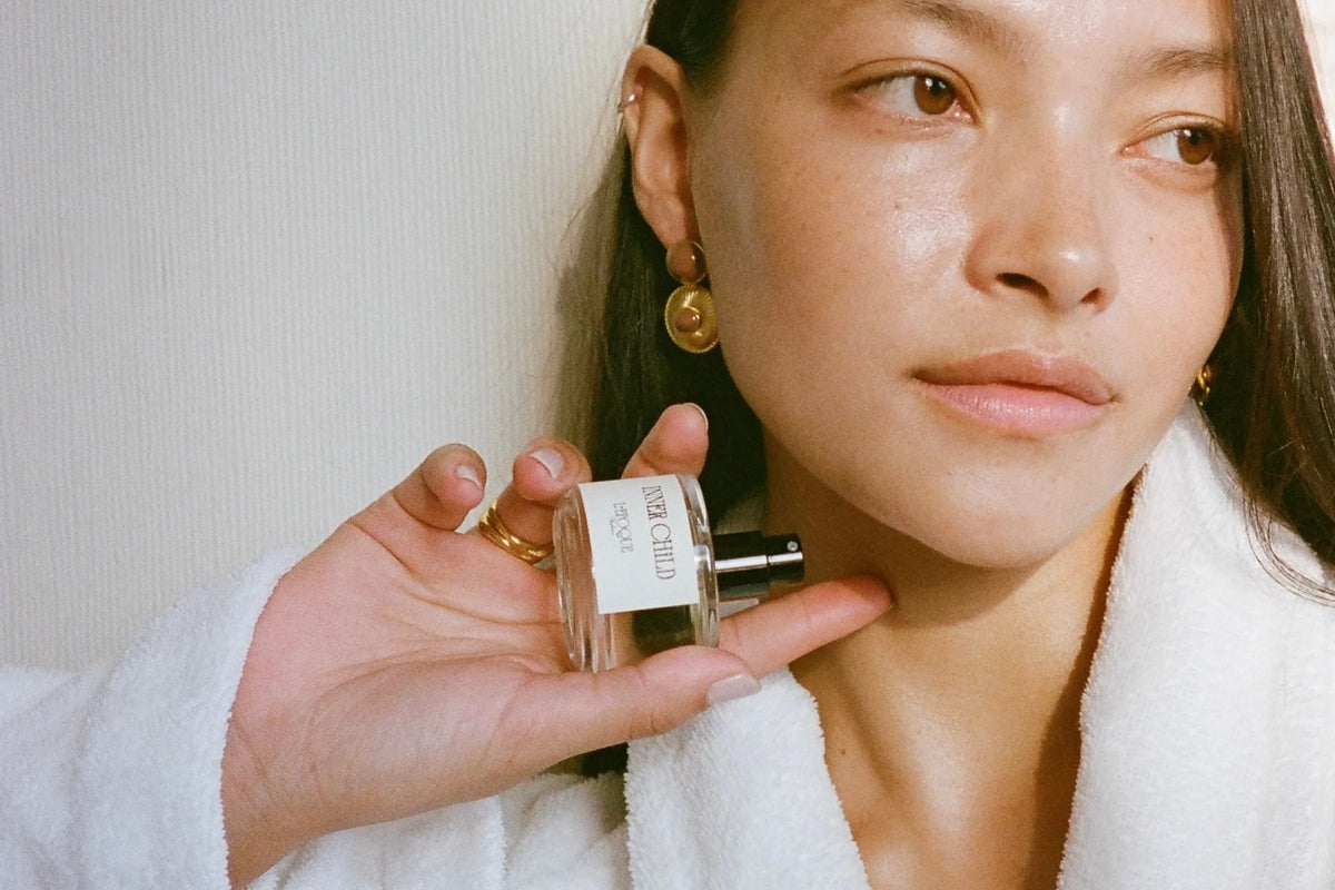 Inner Child eau de parfum 30mL by L'Epoque, held in a manicured hand against a bed of deep red roses