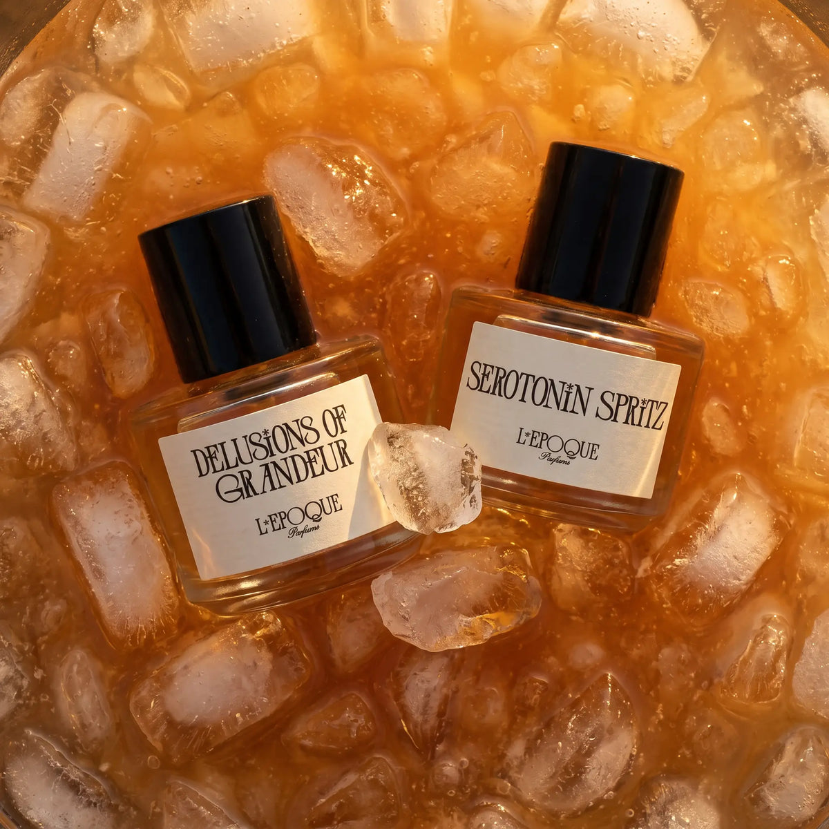 L'Epoque Parfums Jungle Juice duo — Delusions of Grandeur and Serotonin Spritz bottles on ice in an amber cocktail