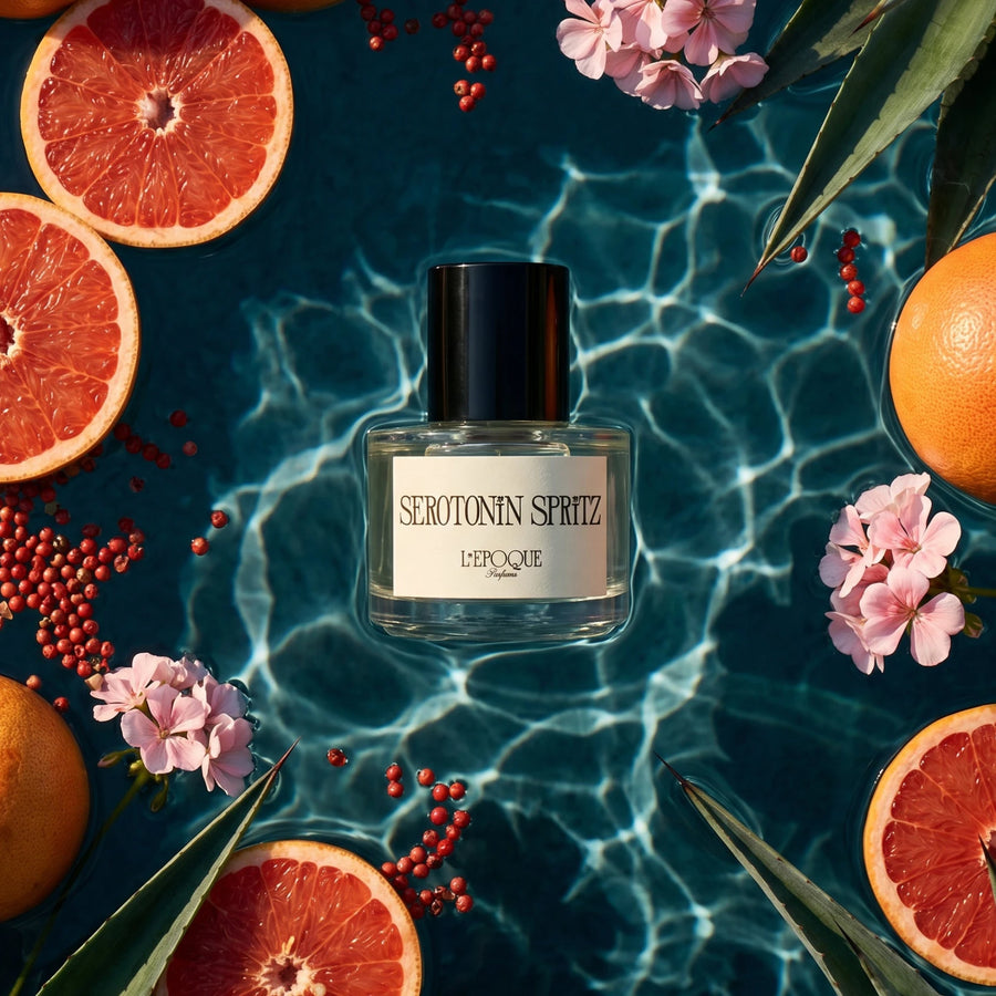 Serotonin Spritz Eau de Parfum by L'Epoque — bottle floating in sunlit blue water surrounded by grapefruit slices, pink peppercorns, and geranium blooms, the fragrance's top and heart notes
