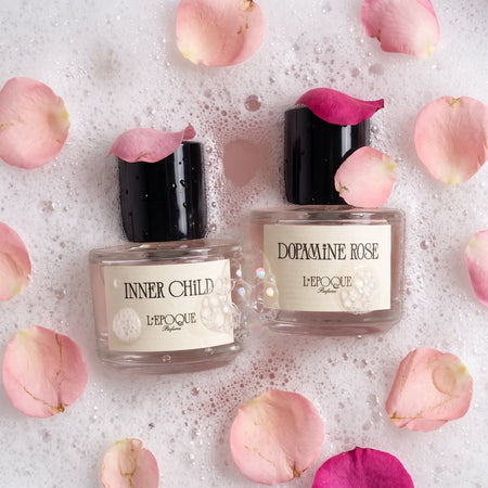 L'Epoque Parfums The Rosewater Bath duo — Inner Child and Dopamine Rose eau de parfum bottles in bubble bath with rose petals