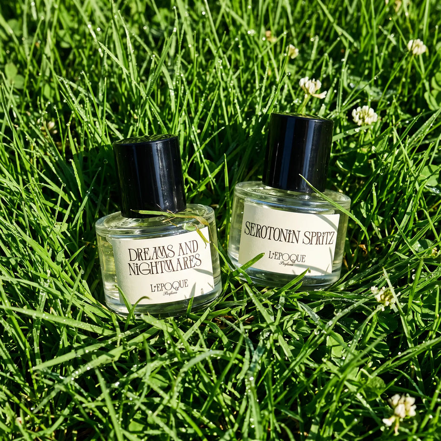 L'Epoque Parfums Touch Grass duo — Dreams and Nightmares and Serotonin Spritz bottles in dewy green grass with clover