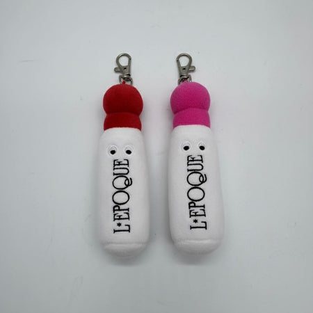 Two white bag charms with red and pink lids labeled 'LEPOQUE' on a white background.