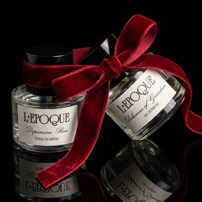 Two perfume bottles with a red ribbon on a black background, featuring the brand 'L'Epoque'.