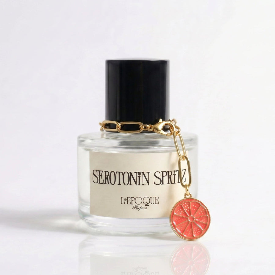 Limited edition grapefruit slice charm on a gold chain clipped to a Serotonin Spritz perfume bottle by L'Epoque