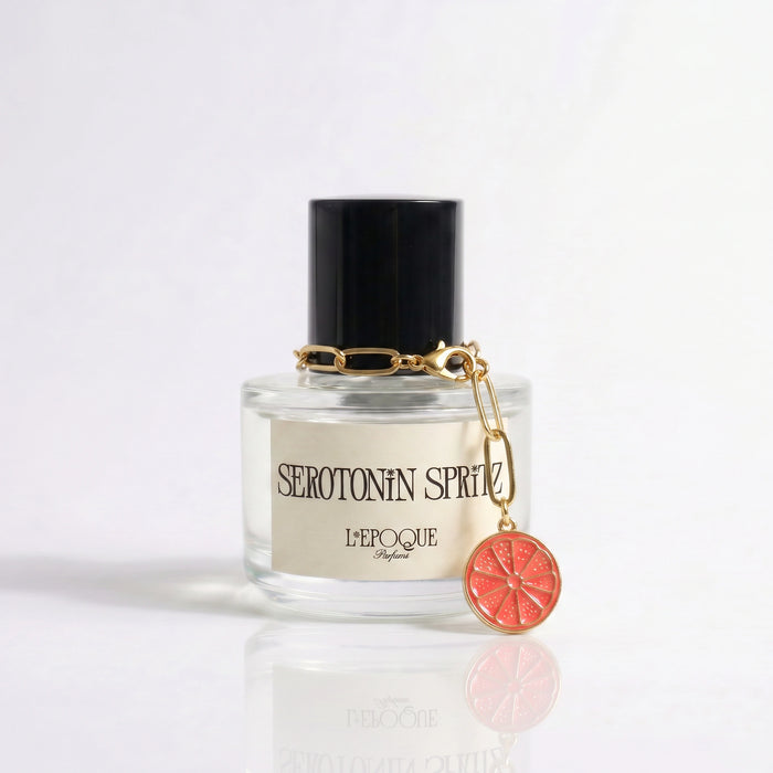Limited edition grapefruit slice charm on a gold chain clipped to a Serotonin Spritz perfume bottle by L'Epoque